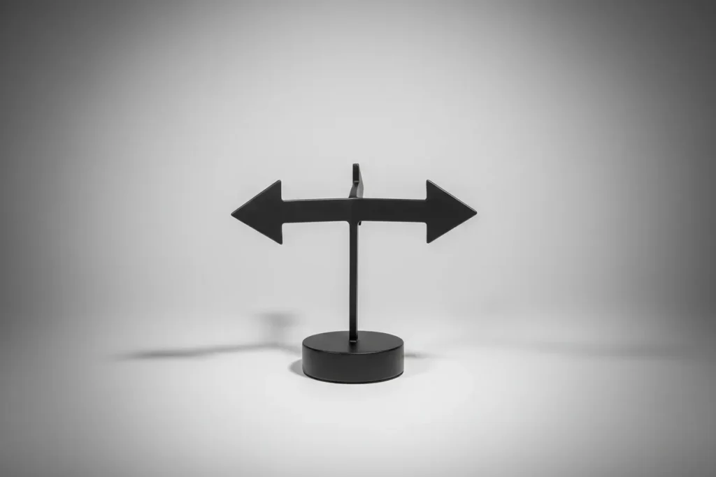 Minimal three-way arrow sculpture on neutral background, symbolizing choice among coaching, role change, or parting ways.