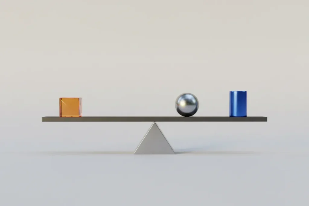 Minimalist balance scale with a sphere, cube, and cylinder balanced on a soft gray background.